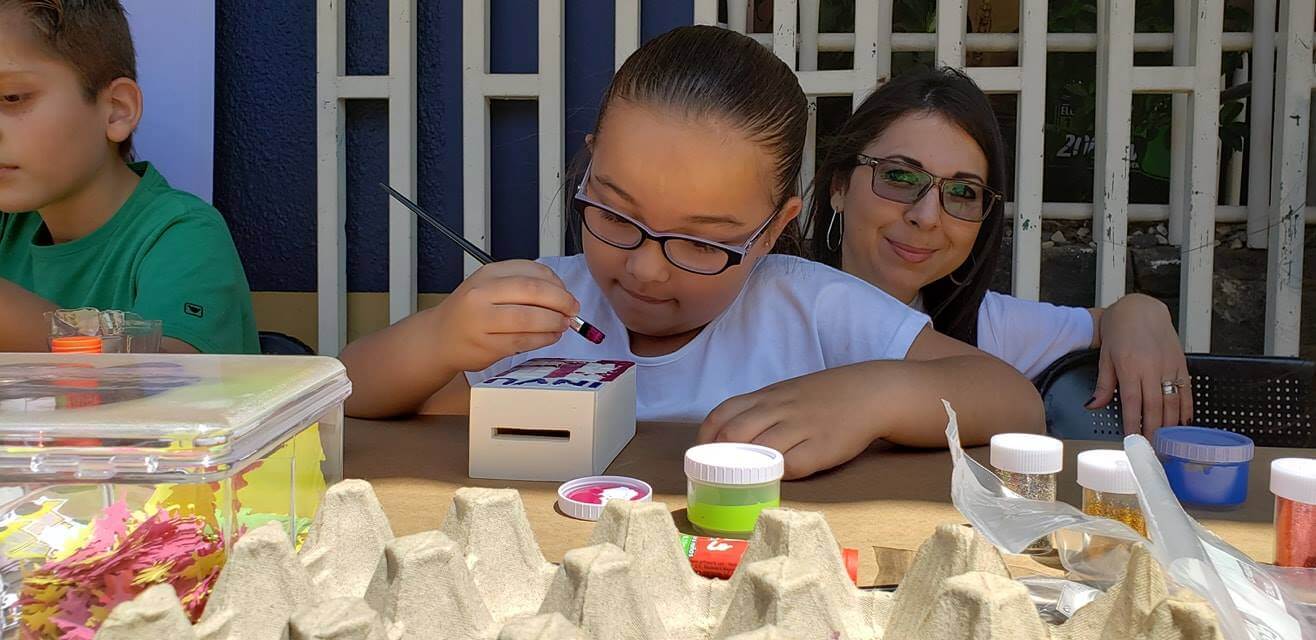 niña pintando una alcancía en forma del edificio del INVU..